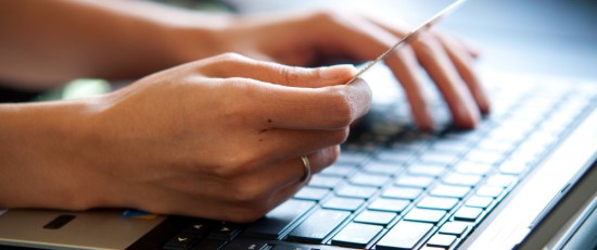 2 Hände die auf einem Laptop Arbeiten und in der Linken Hand hält er ein Dokument