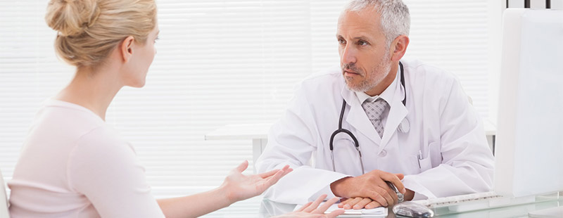 Ein Bild auf diesem ein Arzt und eine Frau sind, beide sitzen sich gegenüber und besprechen etwas.