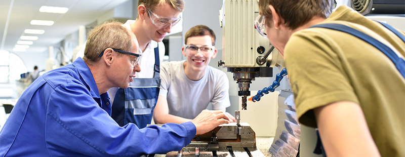 Ein Bild auf dem ein Mann mehreren Personen an einer Maschine etwas erklärt