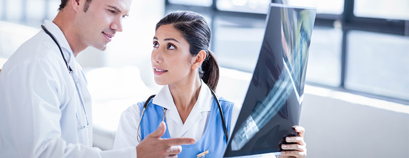 Ein Bild auf dem sich 2 Ärzte Unterhalten und ein Röntgen Bild gemeinsam anschauen