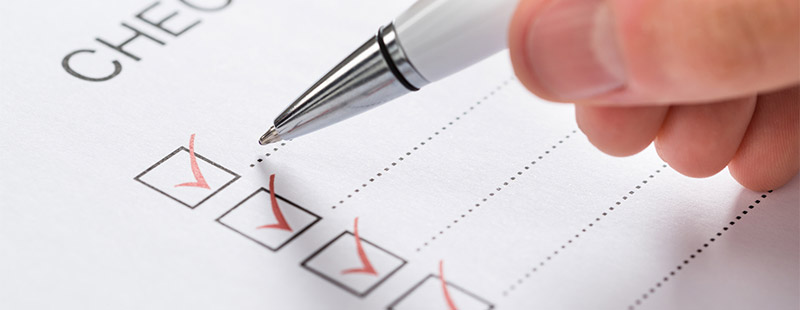 Eine Checkliste auf dem eine Hand gerade mit einem Kugelschreiber rote Haken setzt