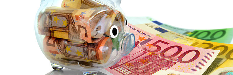 Ein Sparschwein mit Geld gefüllt und neben dem Sparschwein liegen ebenso noch Geldscheine