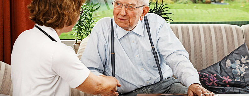 Ein Bild auf dem ein älterer Herr auf dem Sofa sitzt und eine Frau sitzt im Gegenüber sie geben sich die Hand
