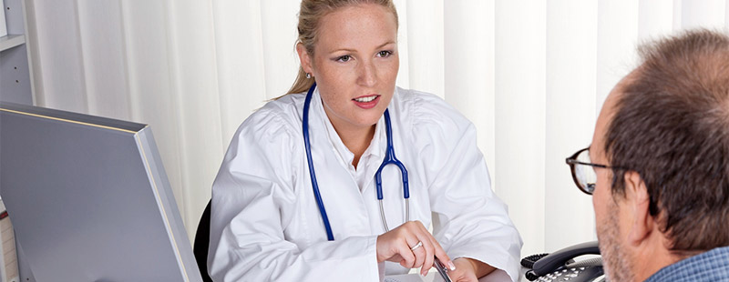 Ein Bild auf dem eine Ärztin zu sehen ist die ein Stethoskop um den Hals trägt und gegenüber sitzt ein Herr mit Brille