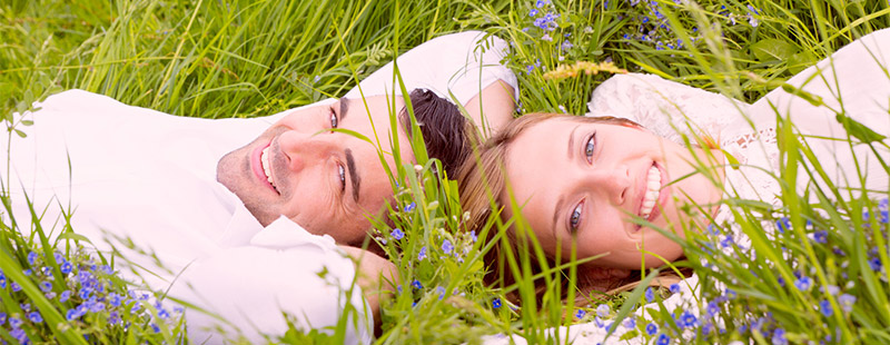 Ein Paar das in einer Grünen Wiese liegt und die Hände hinter dem Kopf haben und lachen