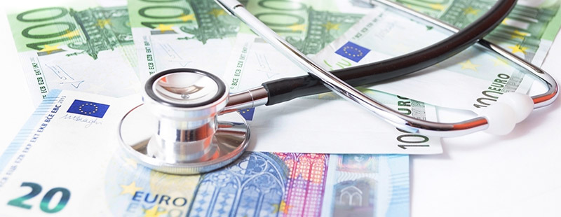 Ein Bild auf dem viele Geldscheine auf dem Tisch liegen und darauf liegt ein Stethoskop