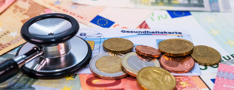 Ein Bild auf dem mehrere Geldscheine eine Gesundheitskarte und Kleingeld zu sehen ist. Ebenso ein Stethoskop Kopf