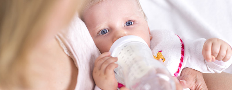 Ein Baby das in den Armen der Mutter liegt und ein Fläschchen bekommt.