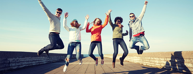 Mehrere Menschen die auf einer Brücke in die Luft springen, im Hintergrund ist Wasser zu sehen