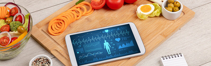 Ein Bild mit Gemüse auf einem Schneidebrett und einem Smartphone das Gesundheitsdaten aufzeigt