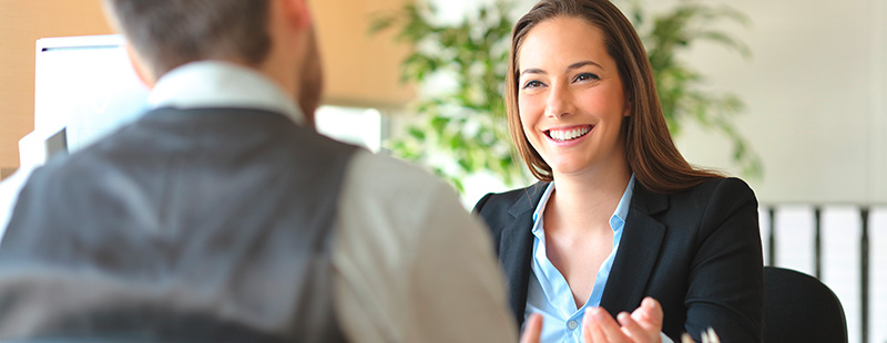 Eine lachende Frau die einem gegenüber sitzenden Mann etwas erklärt
