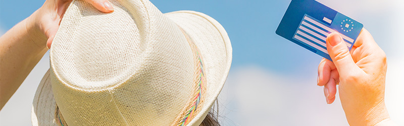 Eine Dame die man von hinten nur mit einem Hut sieht die eine Karte in den Himmel hält (Thema Auslandsversicherung)