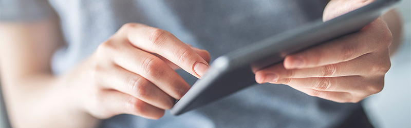 Nahaufnahme von zwei Händen, die ein Tablet halten und mit einem Finger über den Bildschirm wischen.