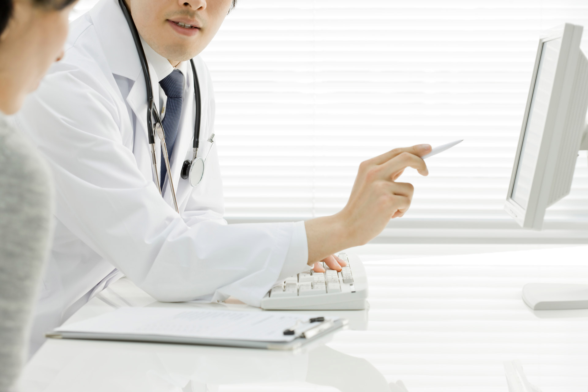 Ein sitzender Mann der mit einem Stift auf einen PC zeigt und einer Dame neben an etwas erklärt.